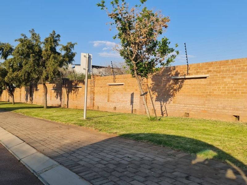 A view of the property's exterior brick boundary wall featuring integrated electric fencing, adjacent to a paved sidewalk and grass verge.