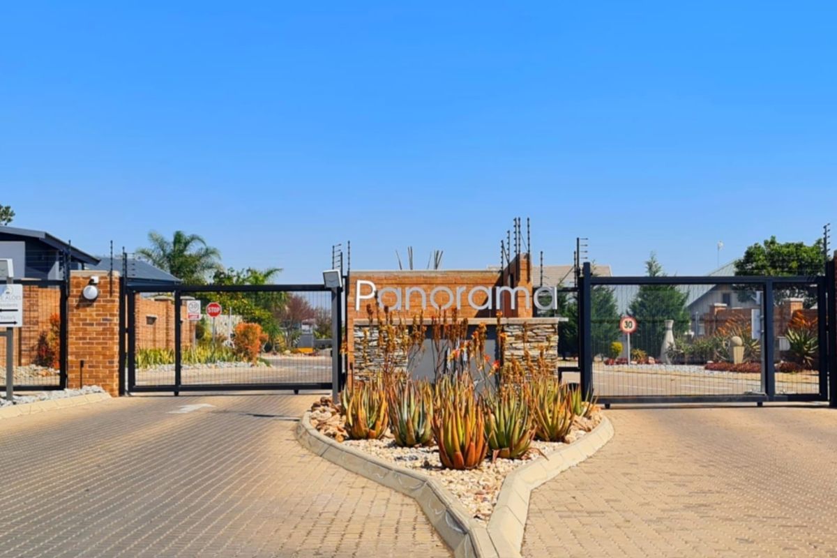 The entrance to Panorama estate featuring a secure gated access point, brick boundary walls, electric fencing, and a paved driveway.