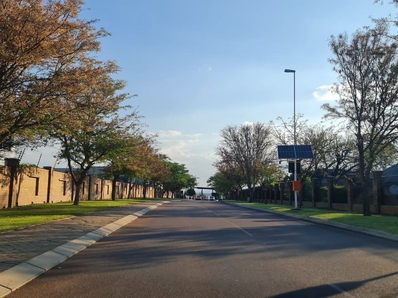 A view of a well-maintained residential street featuring paved roads, brick boundary walls with electric fencing, and solar-powered street lighting.