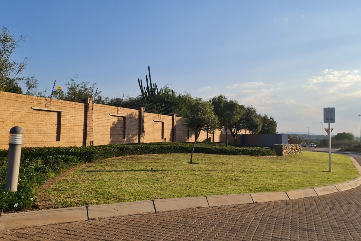 A well-maintained street-facing view featuring a brick boundary wall with electric fencing, manicured lawn, and paved verge.