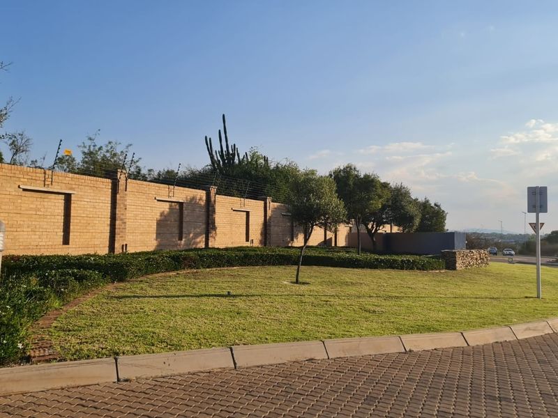 A well-maintained street-facing view featuring a brick boundary wall with electric fencing, manicured lawn, and paved verge.