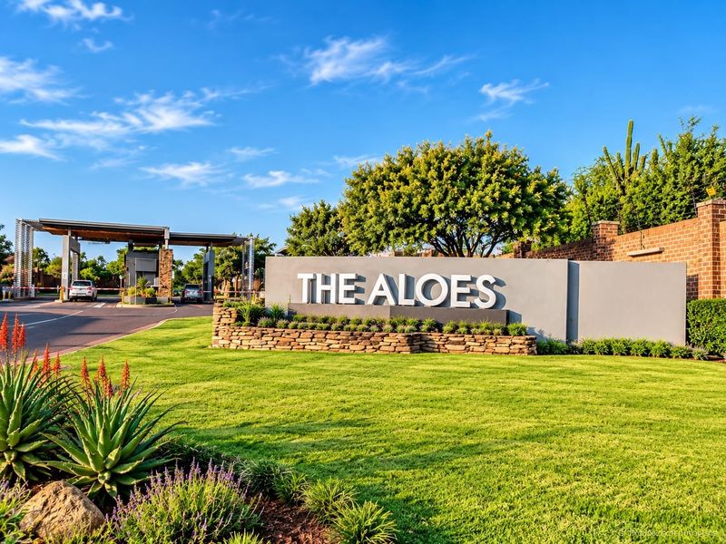 The entrance to The Aloes residential estate, featuring a modern security gatehouse, stone-clad signage wall, and well-maintained landscaped gardens.