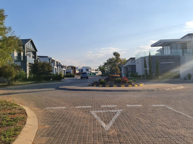 A view of a well-maintained residential street featuring a paved traffic circle and modern homes in a secure estate setting.