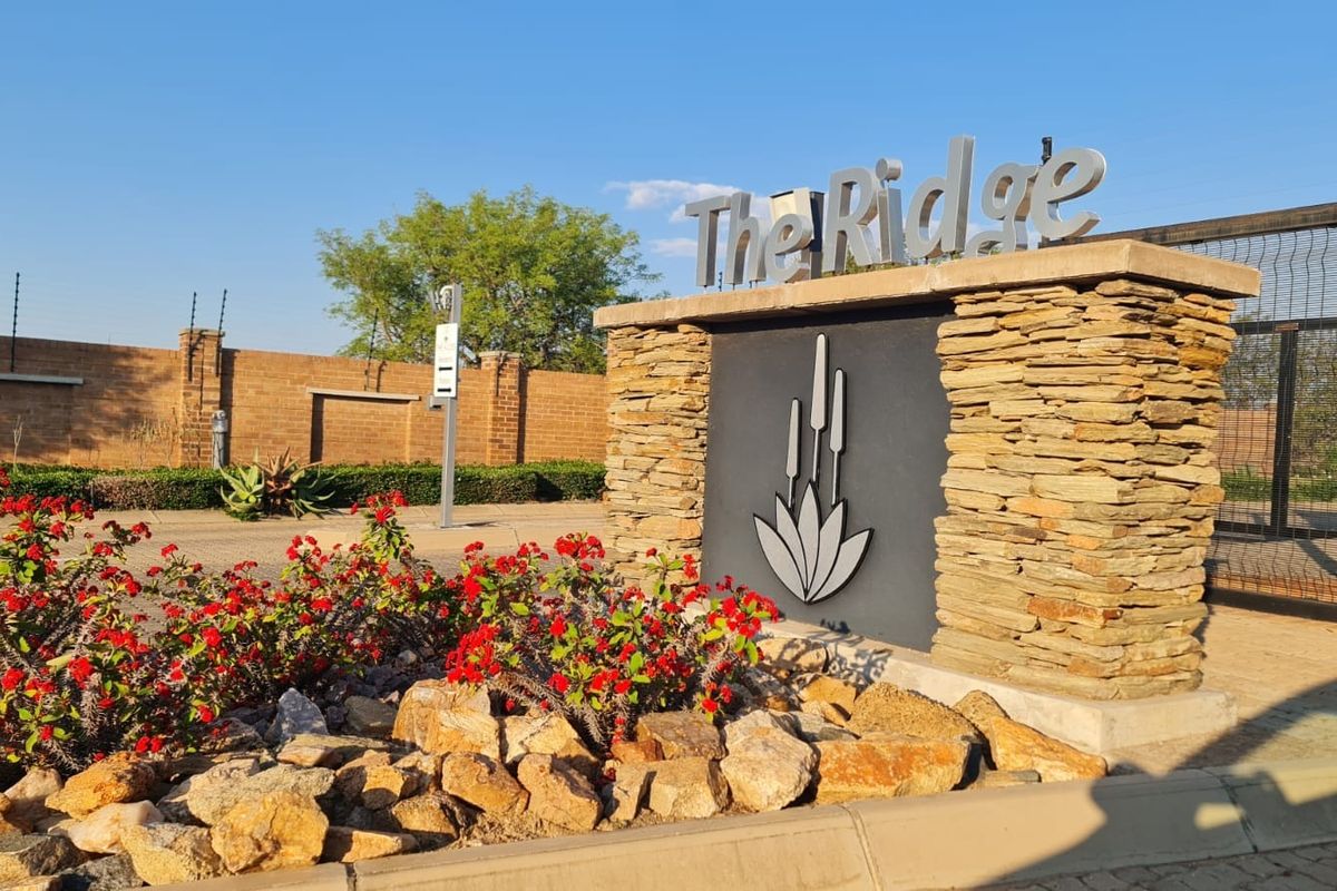 Entrance signage and security perimeter wall for The Ridge residential estate, featuring stone cladding and electric fencing.