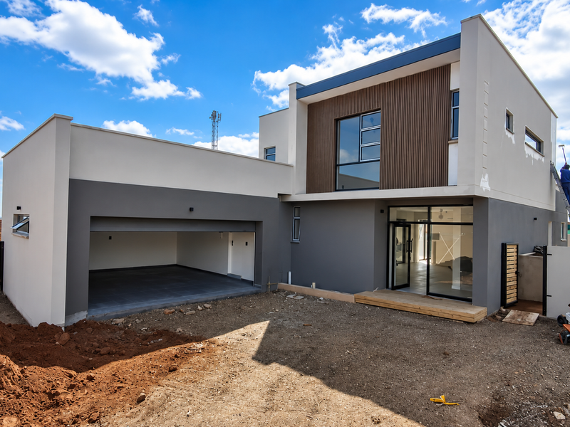 Modern double-story home featuring a double garage, timber cladding accents, and a rear timber deck, currently undergoing final exterior finishing and landscaping.