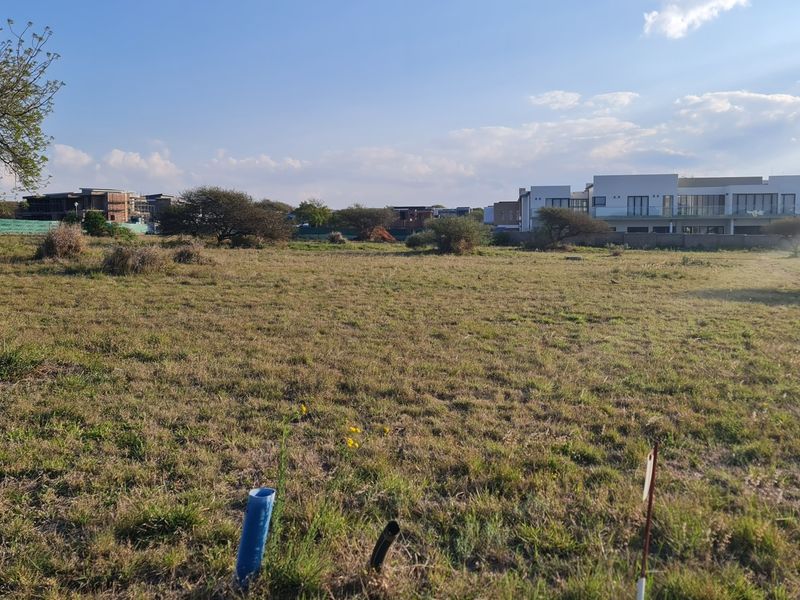 A view of a vacant residential plot featuring natural grass cover and visible utility connection points, situated in a developed residential estate.