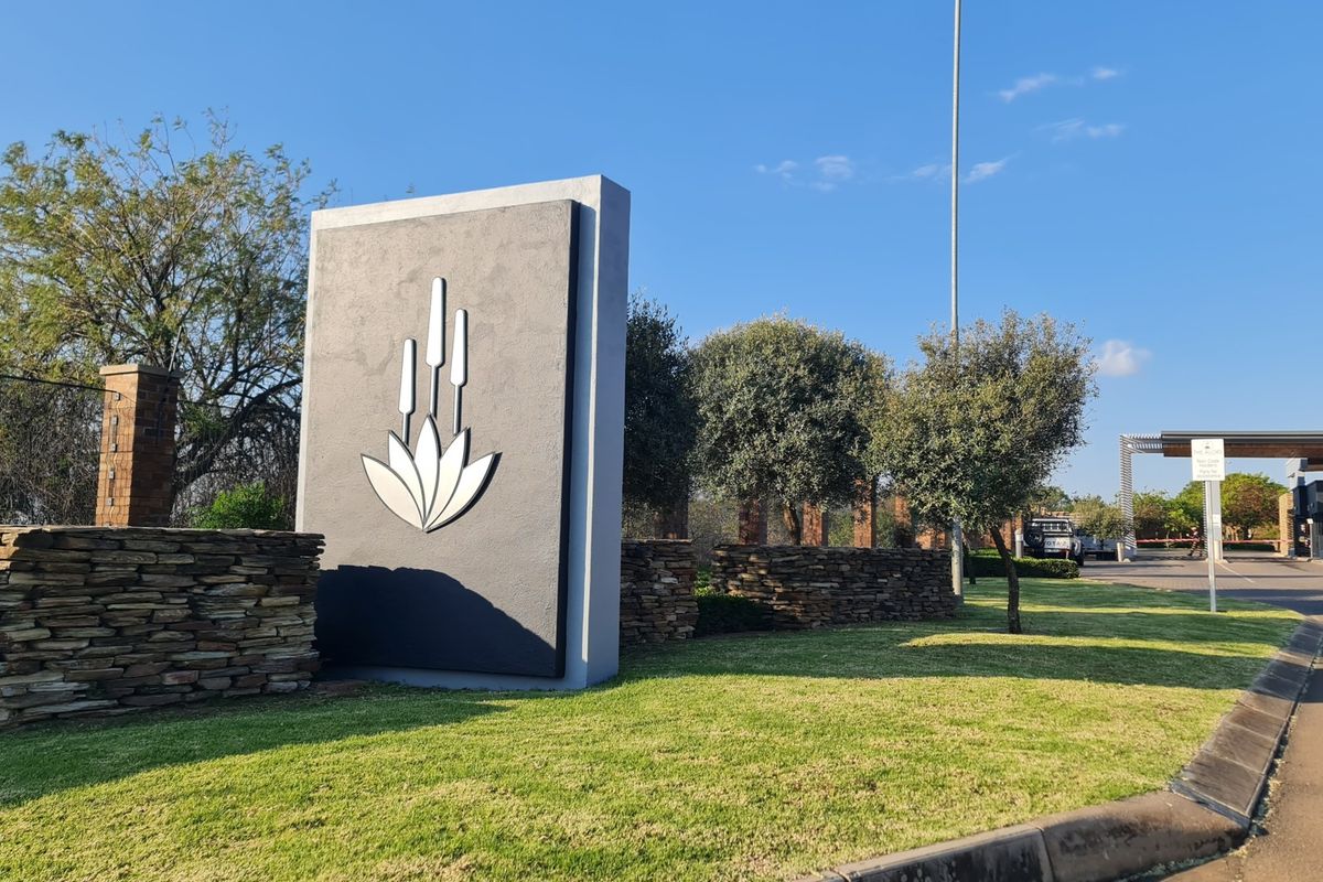 The entrance to the residential estate features a modern stone-clad monument sign, manicured lawns, and established landscaping.
