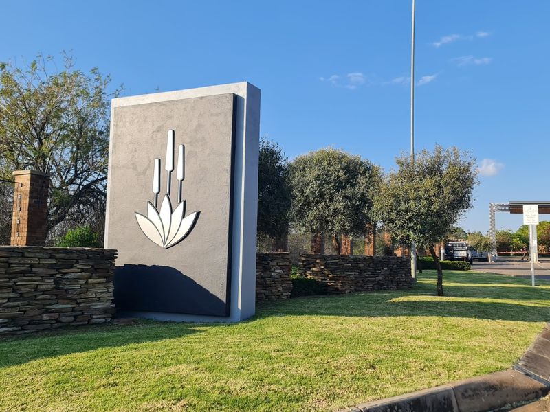 The entrance to the residential estate features a modern stone-clad monument sign, manicured lawns, and established landscaping.