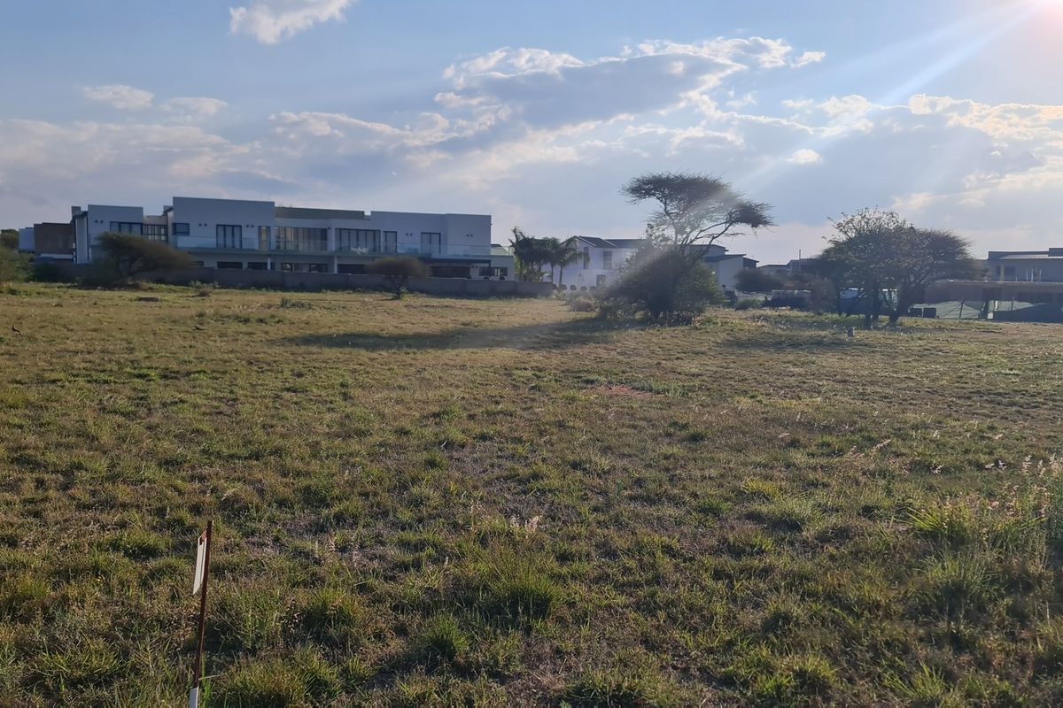 A view of a vacant residential plot of land with surrounding neighborhood development in the background.