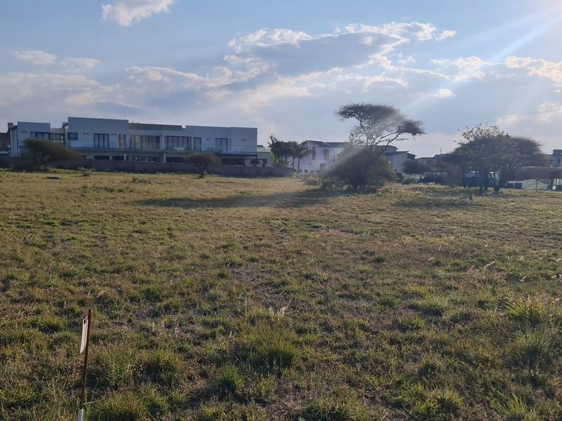 A view of a vacant residential plot of land with surrounding neighborhood development in the background.