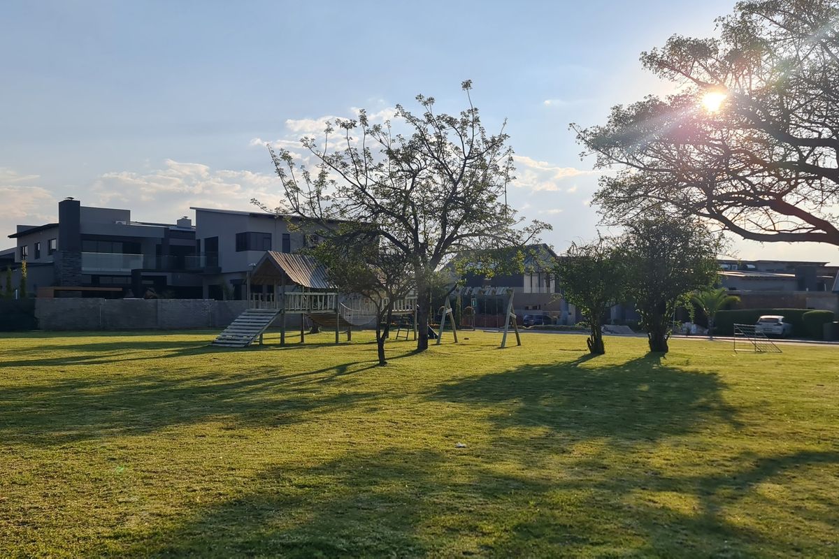 A spacious, well-maintained residential garden featuring mature trees, a manicured lawn, and a secure perimeter boundary wall.