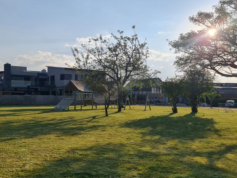 A spacious, well-maintained residential garden featuring mature trees, a manicured lawn, and a secure perimeter boundary wall.