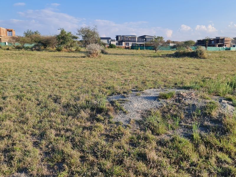 A view of a vacant residential plot of land in a developed estate, featuring natural grass cover and surrounding residential properties.