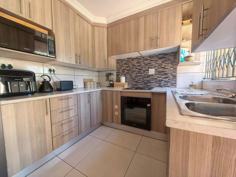 A functional kitchen featuring wood-look cabinetry, mosaic tile backsplash, built-in oven, electric hob, and a double bowl stainless steel sink.