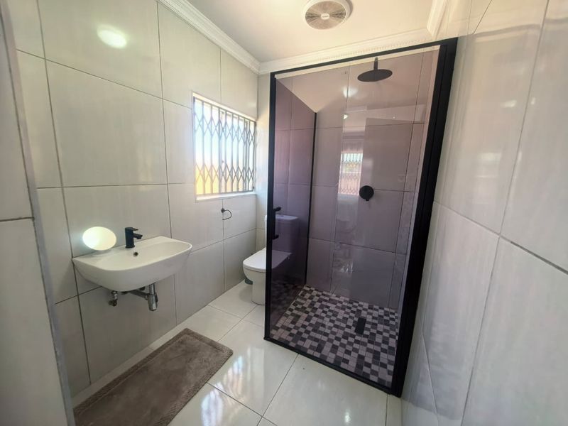 Modern bathroom featuring a wall-mounted basin, a sleek black-framed glass shower enclosure with a rain shower head, and contemporary tiled finishes.