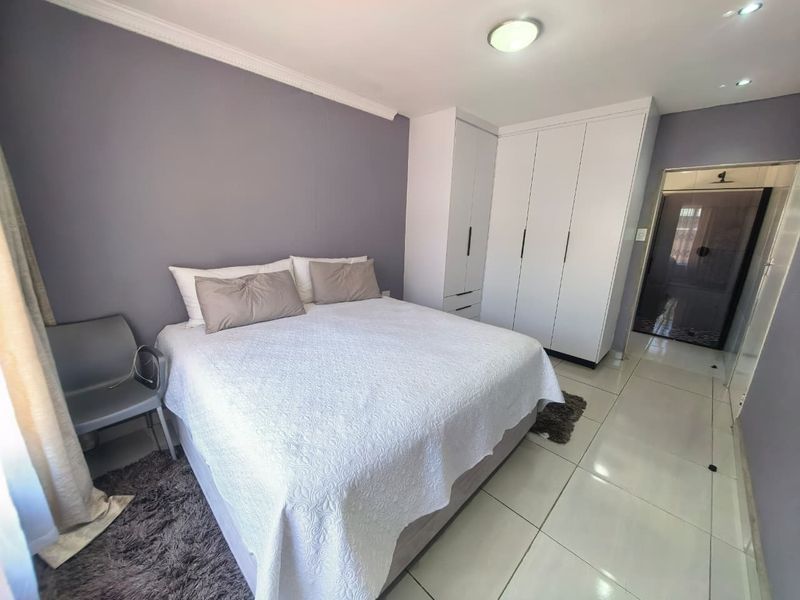 A well-maintained bedroom featuring built-in cupboards, modern tiled flooring, and recessed ceiling lighting, offering a clean and functional living space.