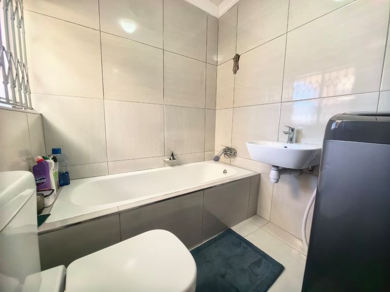 A functional bathroom featuring a bathtub, wall-mounted basin, and toilet with neutral ceramic wall tiling.
