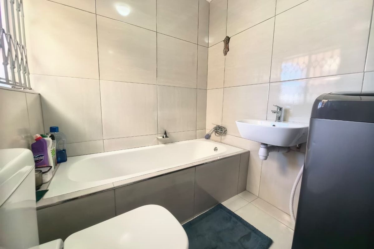 A functional bathroom featuring a bathtub, wall-mounted basin, and toilet with neutral ceramic wall tiling.