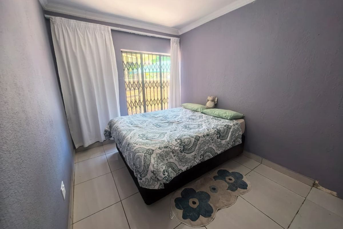 A bedroom featuring tiled flooring, a security gate on the window, and crown molding, providing a functional space with potential for cosmetic updates.