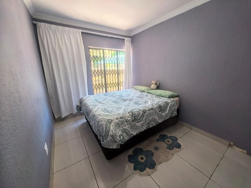 A bedroom featuring tiled flooring, a security gate on the window, and crown molding, providing a functional space with potential for cosmetic updates.