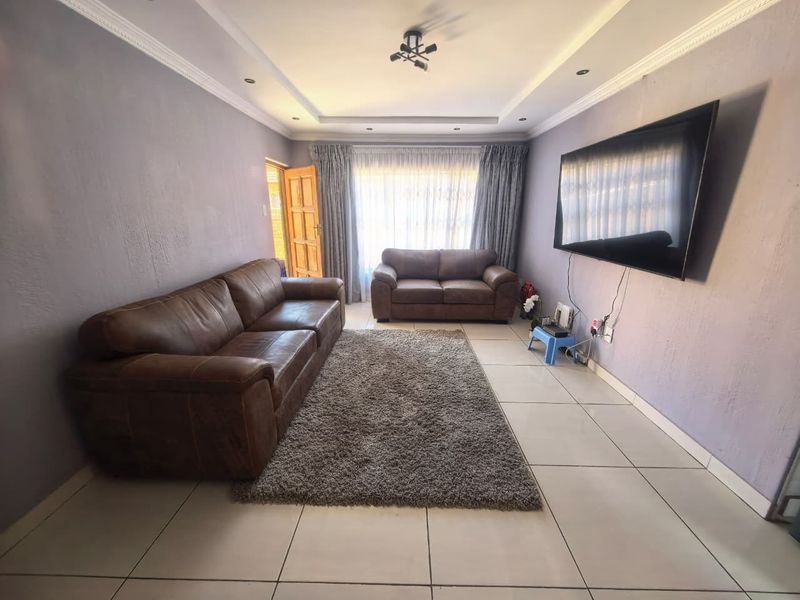 A living room featuring ceramic floor tiles, a recessed ceiling with cove molding, and a sliding door leading to an outdoor area.