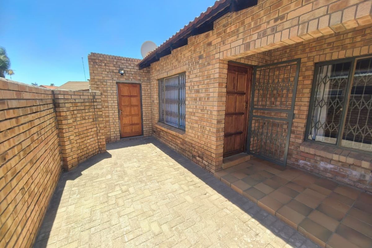 A private rear courtyard featuring face brick walls, paved flooring, and secure access points with security gates and bars.