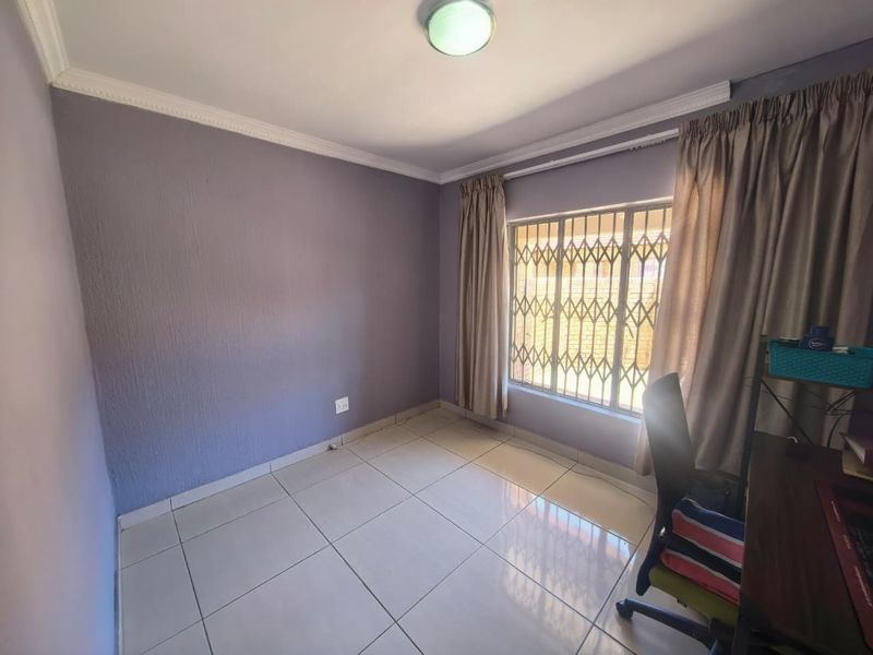 A clean, empty bedroom featuring tiled flooring, a security gate on the window, and classic ceiling cornicing, offering a neutral space ready for personalization.
