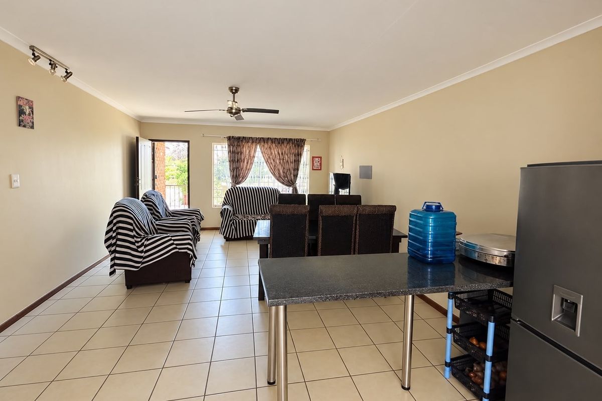 Spacious open-plan living and dining area featuring neutral tiled flooring, a ceiling fan, and a functional granite breakfast counter.