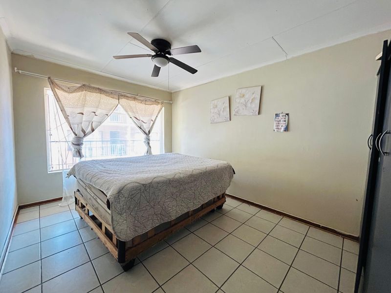 A bedroom featuring tiled flooring, a ceiling fan, and a window with security bars, requiring minor cosmetic updates to improve its overall appeal.