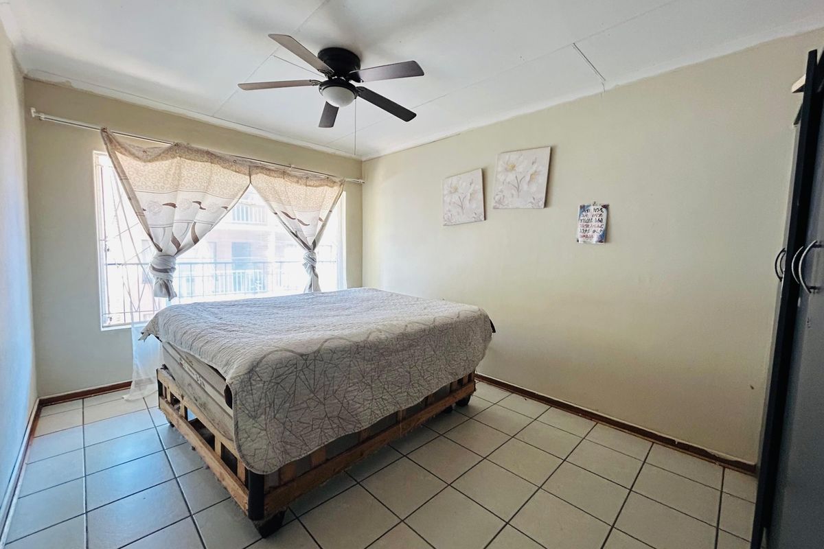 A bedroom featuring tiled flooring, a ceiling fan, and a window with security bars, requiring minor cosmetic updates to improve its overall appeal.