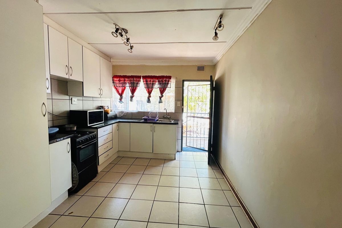 A functional kitchen featuring built-in cabinetry, tiled flooring, and a rear security door, offering a practical layout with potential for cosmetic updates.