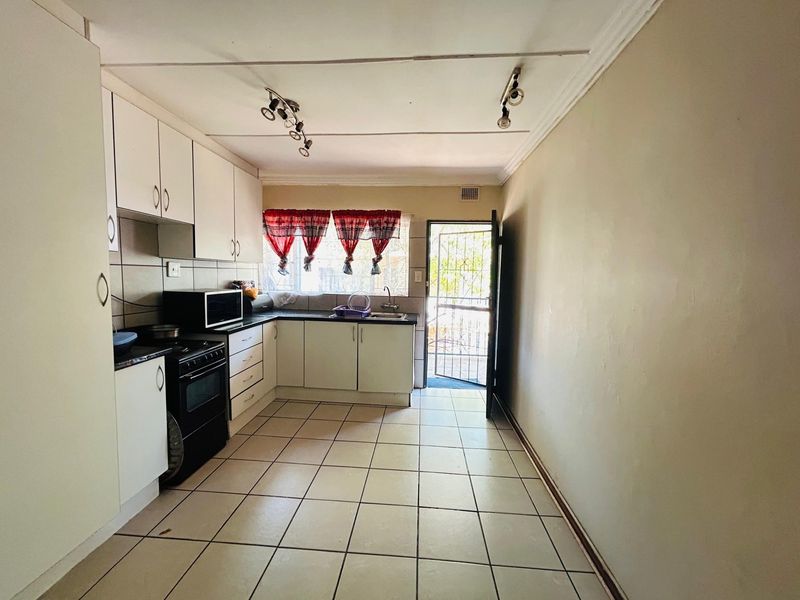 A functional kitchen featuring built-in cabinetry, tiled flooring, and a rear security door, offering a practical layout with potential for cosmetic updates.