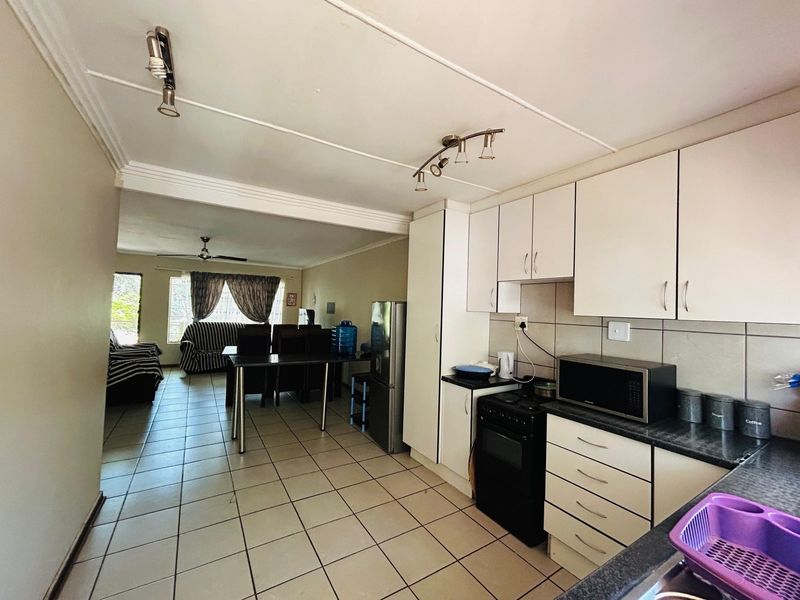 Open plan kitchen and living area featuring tiled flooring, white cabinetry, and functional layout connecting the cooking space to the dining and lounge area.