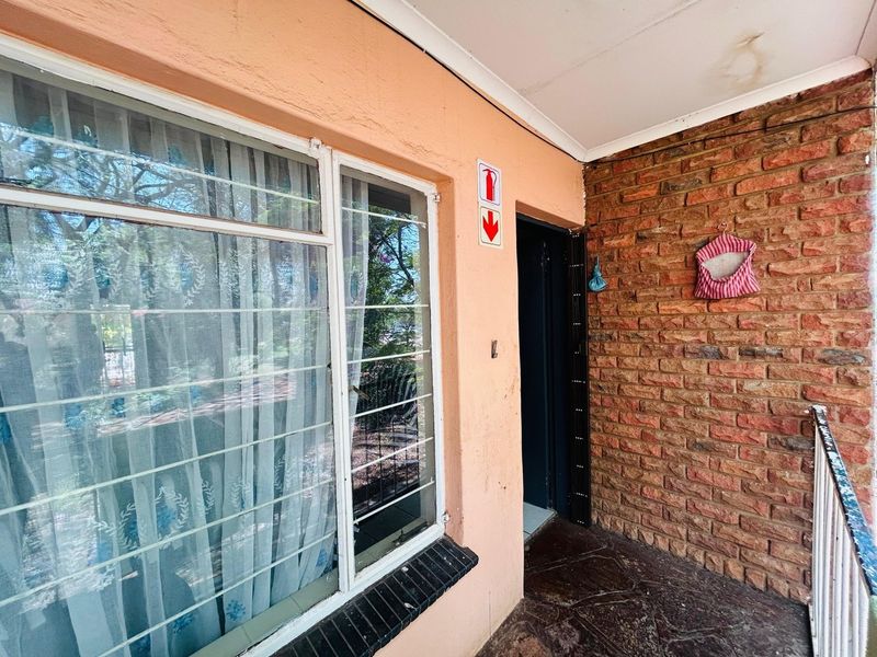 An exterior balcony area featuring a brick feature wall, security window bars, and tiled flooring, showing signs of wear and ceiling staining.