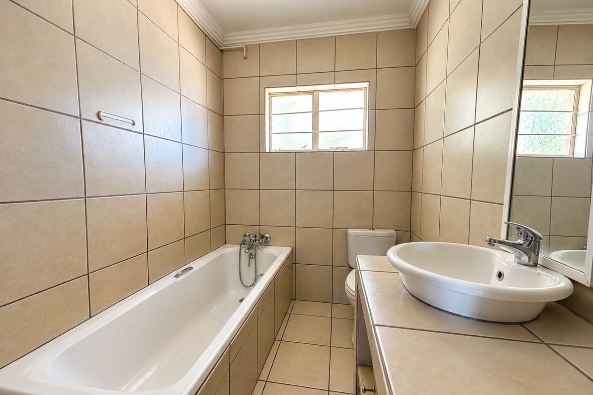 A functional bathroom featuring a built-in bathtub, a vanity basin with a chrome mixer tap, and neutral ceramic tiling throughout.
