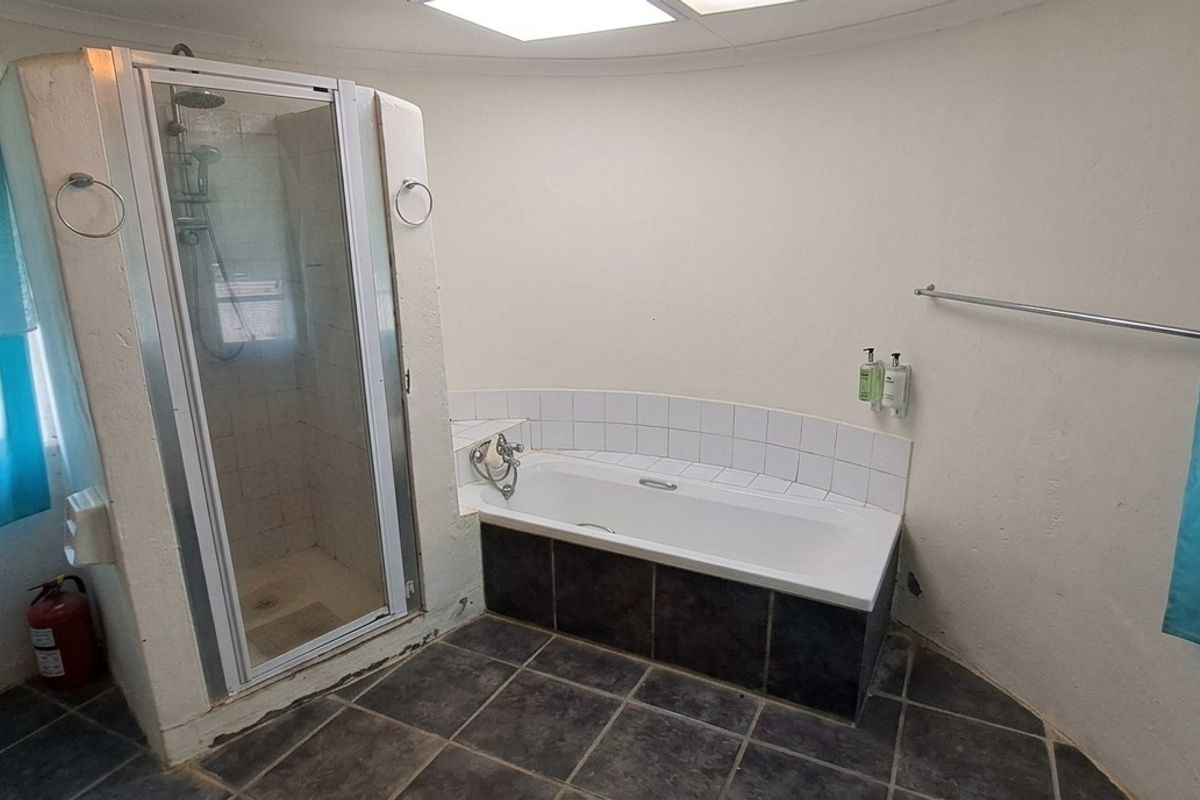 A functional bathroom featuring a separate shower enclosure, a built-in bathtub with tiled surround, and dark floor tiling.