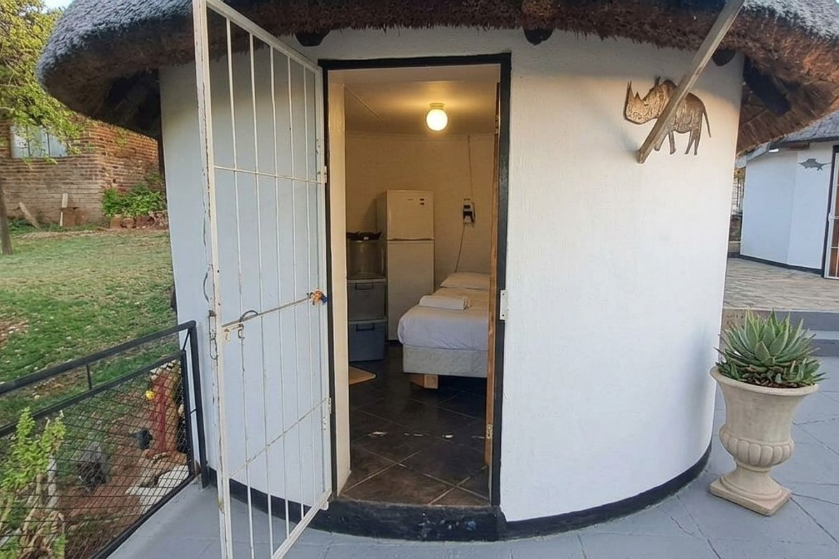 A view of a circular thatched-roof bedroom unit with tiled flooring and a security gate entrance, situated on a paved patio area.