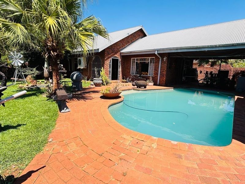 Outdoor entertainment area featuring a swimming pool, brick paved patio, and a covered veranda adjacent to the main brick residence.