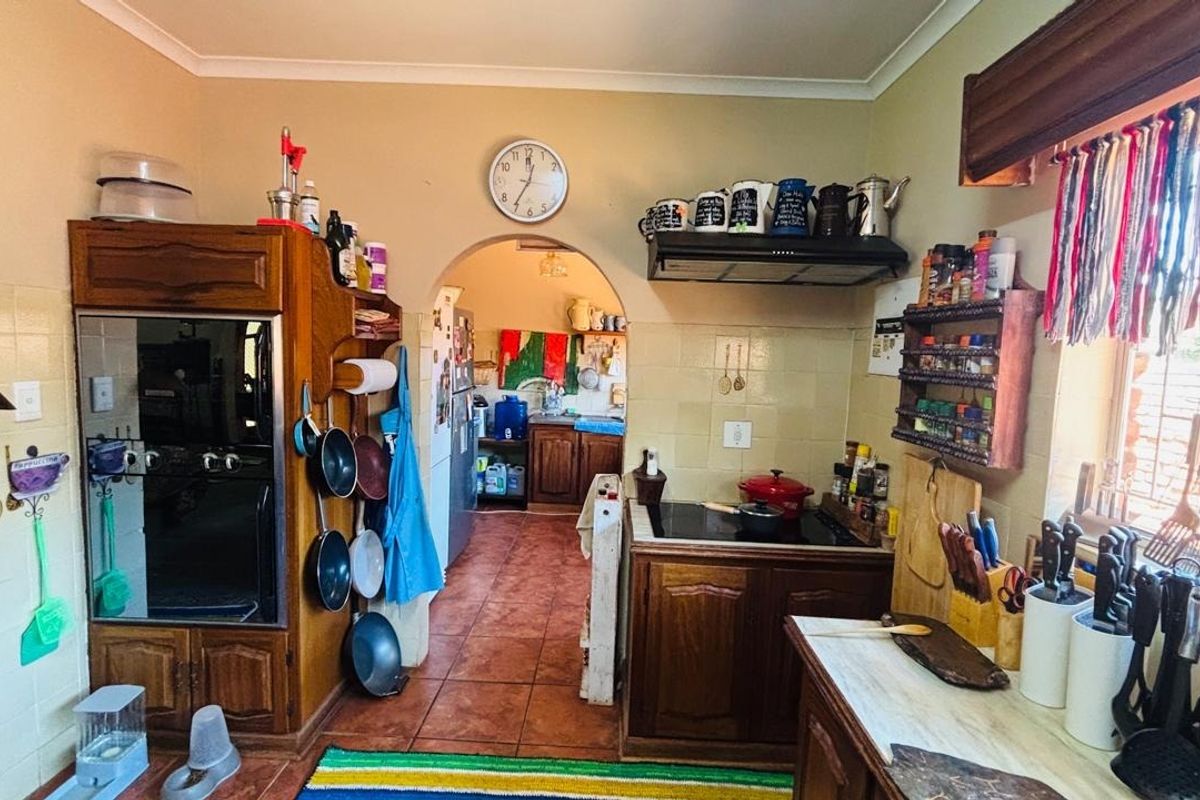 A functional kitchen featuring wooden cabinetry, built-in oven, hob with extractor fan, and tiled splashbacks, leading through an archway to a secondary prep area.