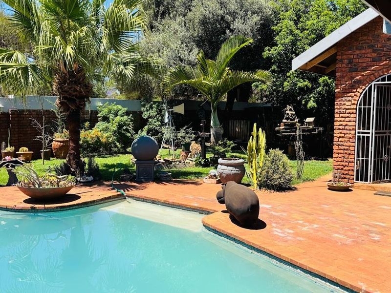 A well-maintained outdoor pool area featuring a brick-paved patio, a swimming pool, and a charming brick building with an arched entrance.