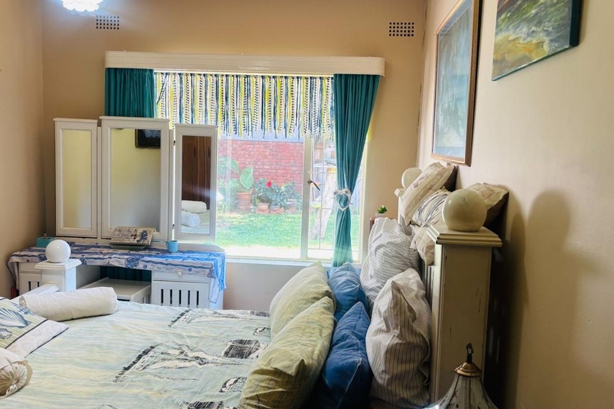 A bedroom featuring a large sliding window with garden views, neutral wall finishes, and integrated ventilation grilles.