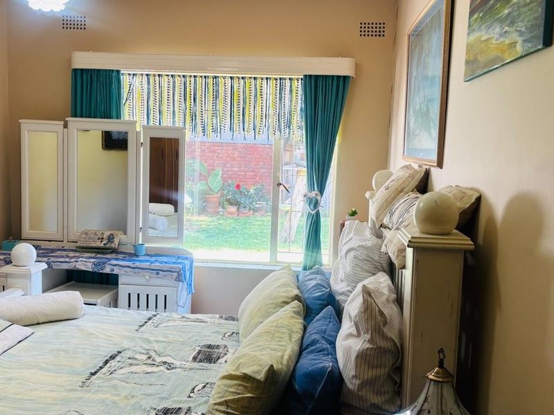 A bedroom featuring a large sliding window with garden views, neutral wall finishes, and integrated ventilation grilles.