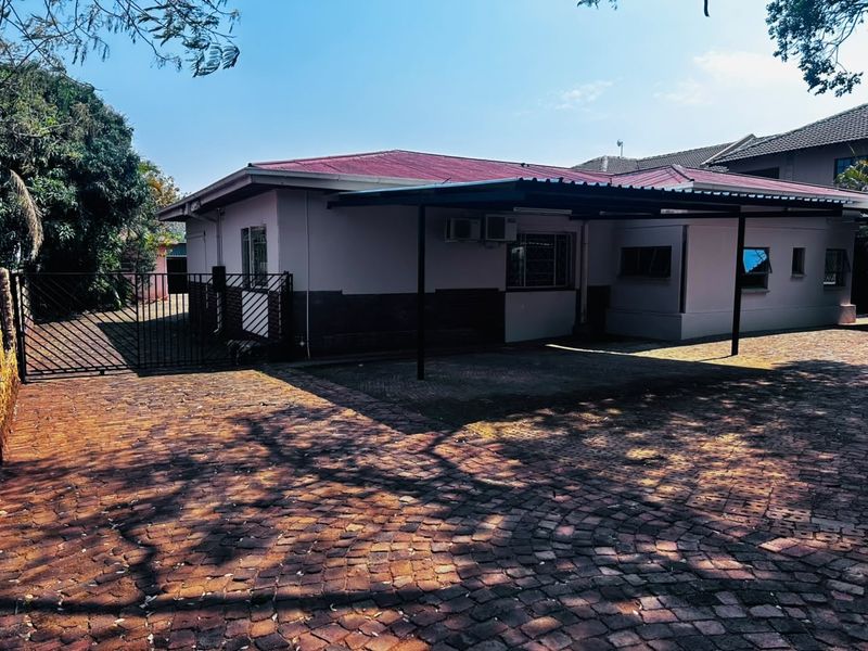 Front exterior view of the house featuring a paved driveway, a covered carport, and secure metal gate access.