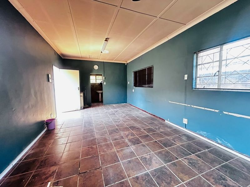 An empty living area featuring tiled flooring, security bars on windows, and ceiling panels, requiring cosmetic updates to the wall finishes.