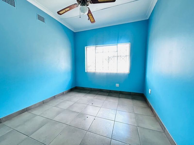 An empty bedroom featuring blue painted walls, tiled flooring, and a ceiling fan, providing a blank canvas for personalization.