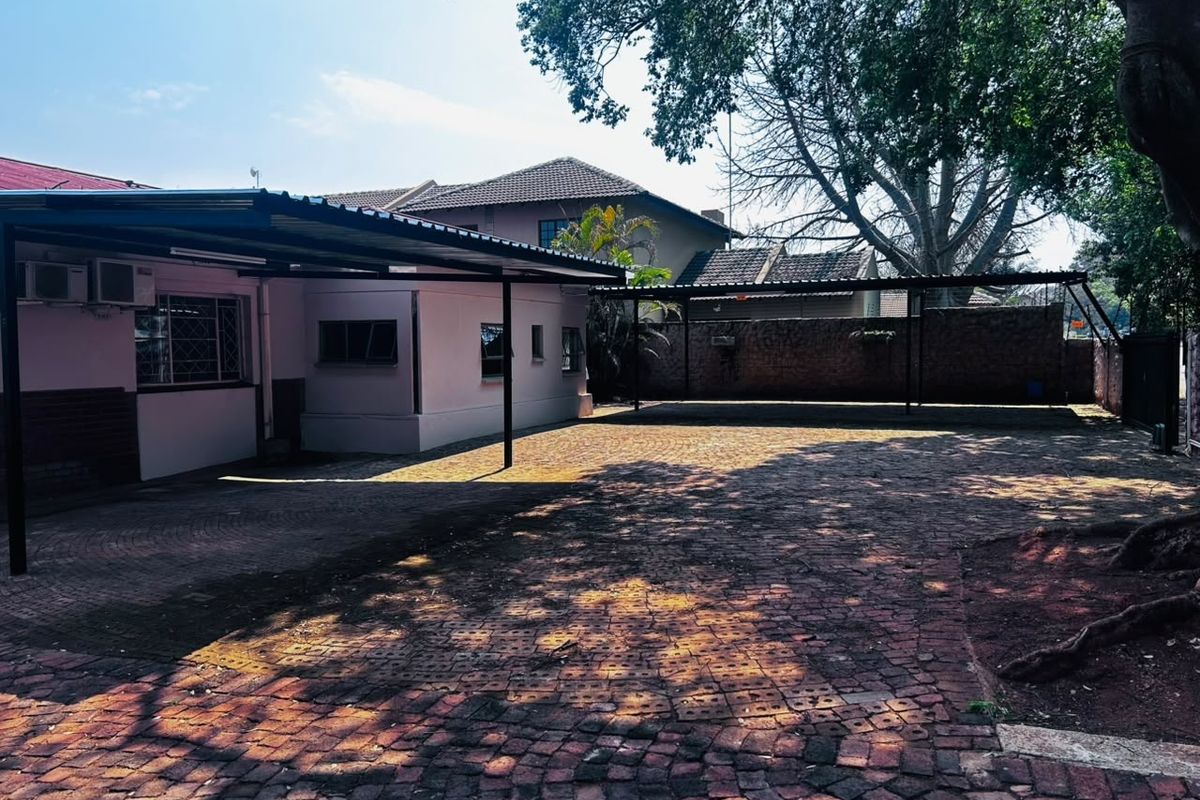 Spacious paved rear courtyard featuring a large covered carport area and secure brick boundary walling.