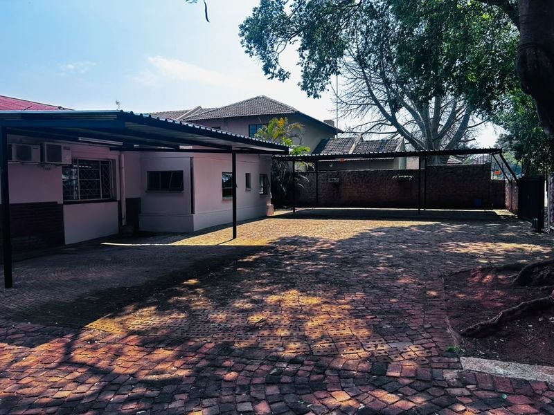 Spacious paved rear courtyard featuring a large covered carport area and secure brick boundary walling.