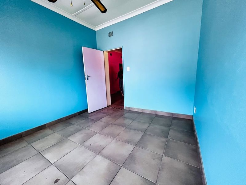 An empty bedroom featuring blue painted walls, tiled flooring, and a ceiling fan, offering a blank canvas for potential interior updates.