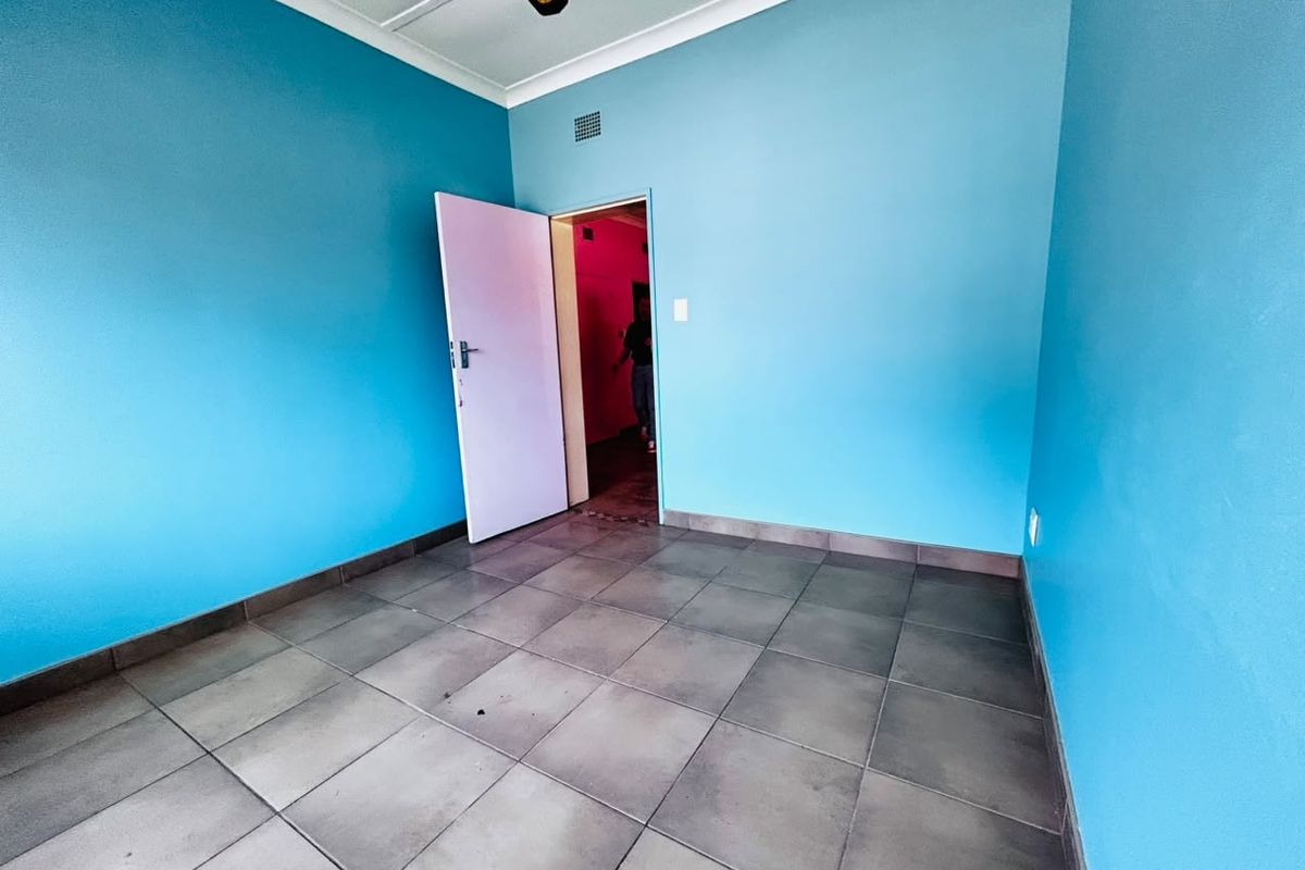 An empty bedroom featuring blue painted walls, tiled flooring, and a ceiling fan, offering a blank canvas for potential interior updates.
