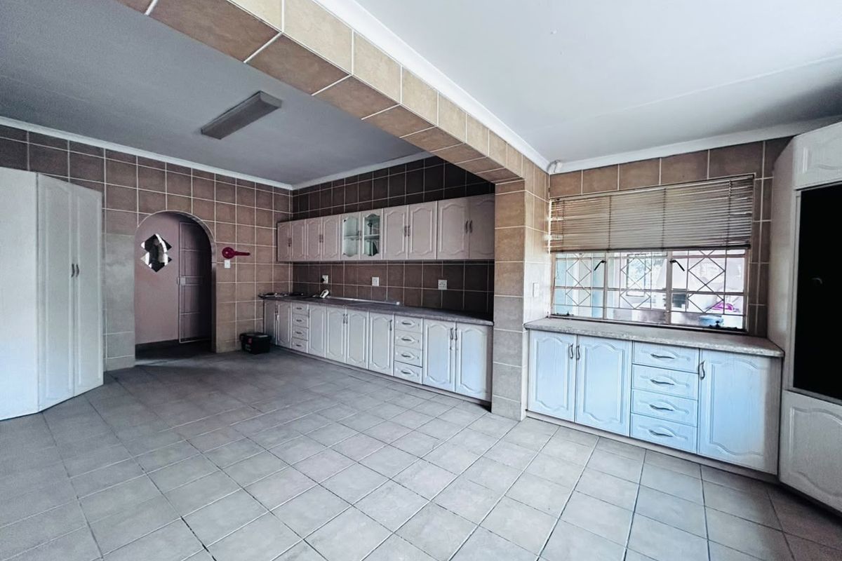 Spacious kitchen featuring extensive built-in cabinetry, tiled walls and flooring, and a distinct architectural archway, offering a blank canvas for modern renovation.